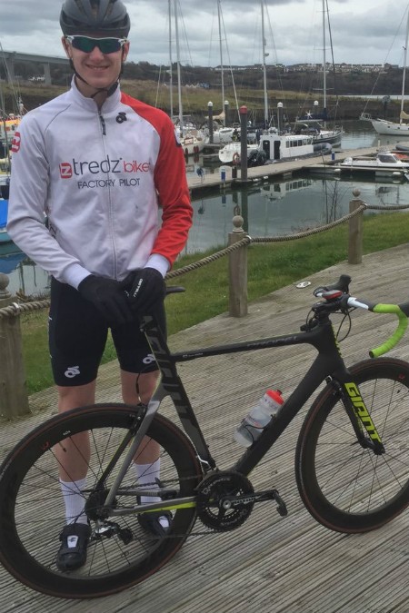 Ieuan in a habour posing for a photo in front of the boats with his road bike